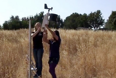 Two people raising an anemometer mast in an open field