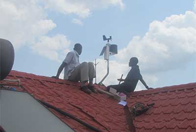 Two people installing a personal weather station on a tiled rooftop